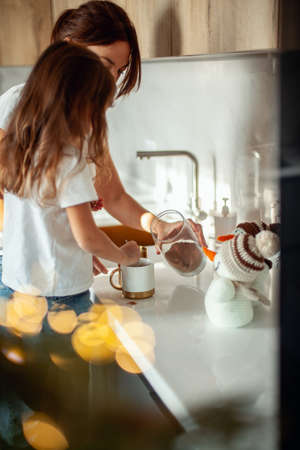 A young beautiful mother and a crying daughter are preparing cocoa in a stylish home kitchen.の写真素材