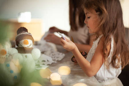 Little cute girl cuts snowflakes from white paper. Gingerbread and cocoa with marshmallows. The concept of preparation for the New Year and Christmas.の写真素材