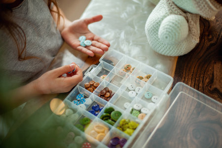 Little cute girl chooses buttons for knitted snowmen. New Years decor is on the table. Preparation for Christmas concept.の写真素材