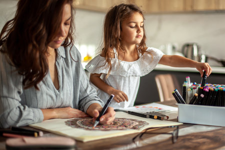 Young beautiful mother and cute daughter draw a mandala pattern together. Artistic markers and colored pencils.の写真素材