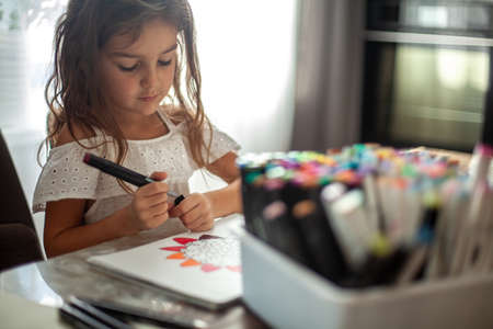 A little cute girl draws a circular mandala pattern in the album with art markers.の写真素材