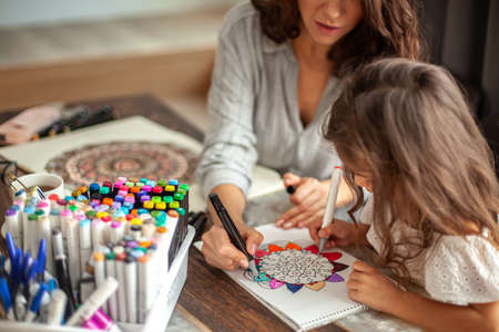 Young beautiful mother helps her daughter to draw a big flower in the style of zen drawing. Circular mandala.の写真素材
