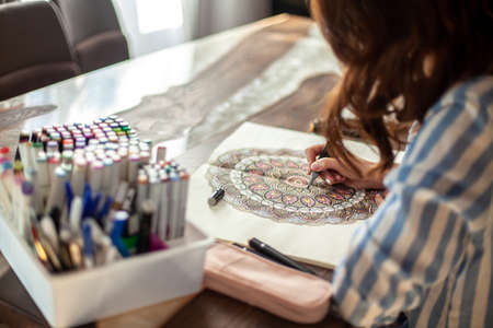 Young beautiful woman is sitting in the home kitchen and drawing a coloring mandala. Zen drawing.の写真素材