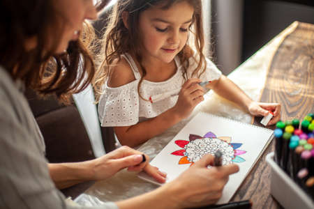Young beautiful mother helps her daughter to draw a big flower in the style of zen drawing. Circular mandala.の写真素材