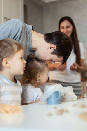 Mom, dad and children decorate Christmas gingerbread at home. A boy and a girl paint with cornets with sugar icing on cookies. New Years decor, branches of a Christmas tree.の写真素材