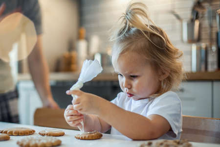 Little cute girl decorates gingerbread with sugar icing. Preparation for Christmas concept.の写真素材
