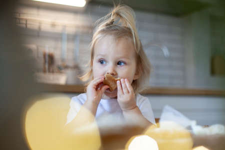 Little cute girl decorates and eating gingerbread with sugar icing. Preparation for Christmas concept.の写真素材
