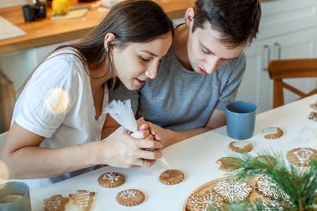 Beautiful man and woman decorate Christmas gingerbread. Two people draw a heart on the cookie. Stylish home kitchenの写真素材