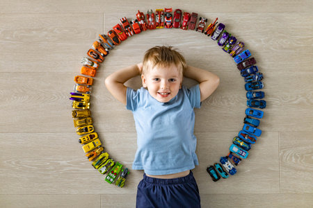 Laughing little cute baby boy lying in circle of car model toys hot wheels collection top viewの写真素材