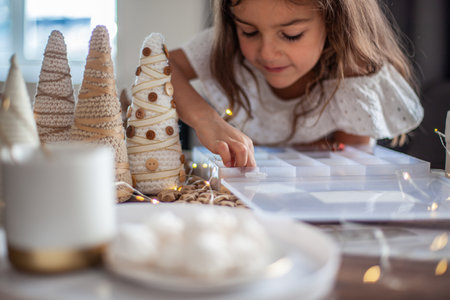 Cute little girl with curly hair making crafts and decorating Christmas Tree cone with buttons.の写真素材