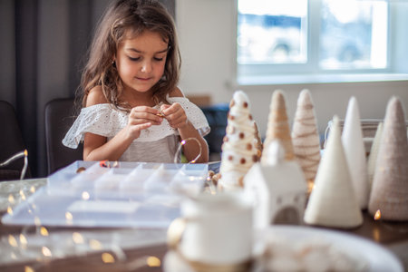 Cute little girl with curly hair making crafts and decorating Christmas Tree cone with buttons.の写真素材