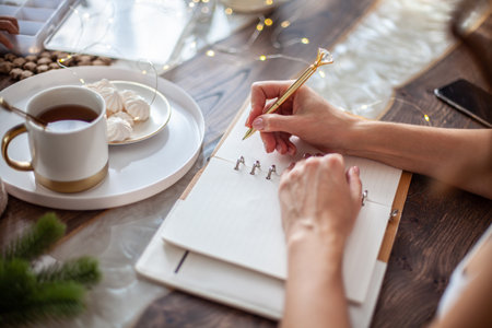 Young woman writing plans or goals for New Year 2021 while her daughter crafting Christmas treesの写真素材