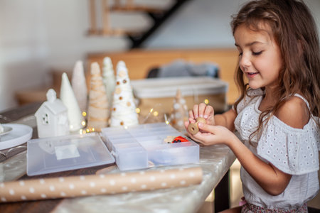 Cute little girl with curly hair making crafts and decorating Christmas Tree cone with buttons.の写真素材