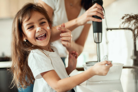 Mom and daughter prepare icing for gingerbread in their home kitchen. Beat with a blender. The girl helps the woman.の写真素材