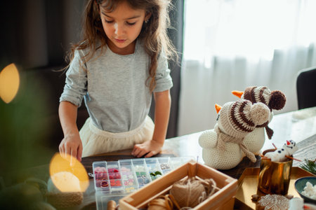 Little cute girl chooses buttons for knitted snowmen. New Years decor is on the table. Preparation for Christmas concept.の写真素材