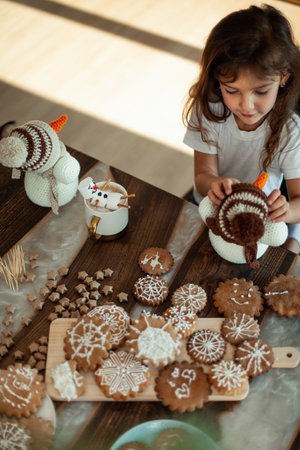 Little cute girl plays with knitted snowmen and eats gingerbread and drinks cocoa with marshmallows.の写真素材