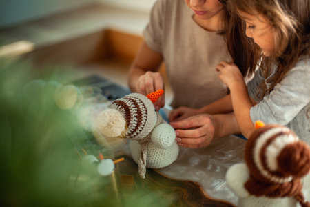 Little cute girl and young beautiful woman make knitted snowmen. Mom and daughter are sewing on buttons.の写真素材