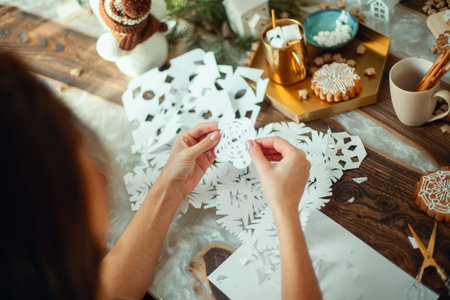 Little cute girl and young beautiful woman cut snowflakes from white paper. Gingerbread and cocoa with marshmallows.の写真素材