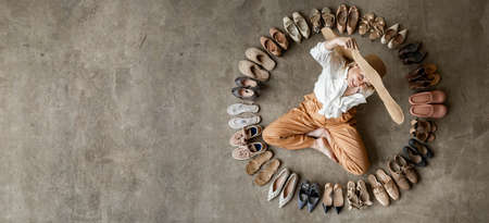 Top view stylish blonde female posing choosing shoes sitting on floor. Top view many female shoes on...