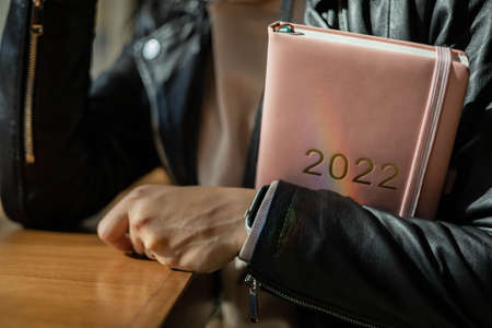 Inspired young woman with a smile looking through window and holding coral colored diary 2022の写真素材
