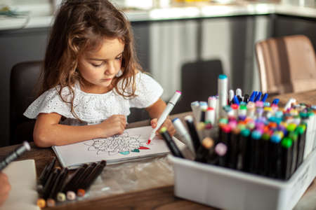 A little cute girl draws a circular mandala pattern in the album with art markers.の写真素材