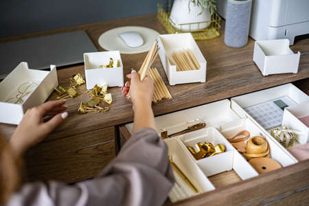 A woman is cleaning up her white workplace. Neatly arranged gold stationery. Storage method.の写真素材
