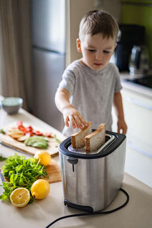 Cute male baby cooking fresh hot sandwiches with cheese, fruits and berries frying bread use toaster