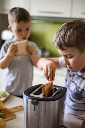 Two funny little brothers cooking and eating together fresh frying bread use toaster at kitchen