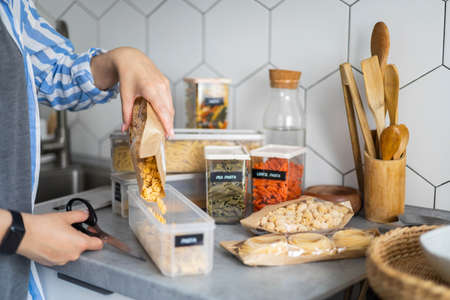 Closeup female hands placing and sorting pasta into pp boxes. Storage organization at kitchen