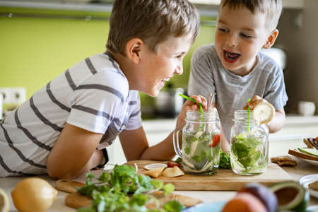 Two laughing little boys drinking refreshing vitamin summer cocktail from jar use straw having funの写真素材