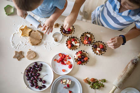 Top view two male children cooking fresh summer dessert with dough and ripe fruits berries