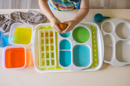 Cute baby boy learning mixing different colors with water and paint in containers. Early development