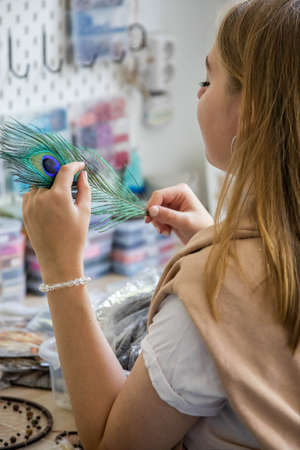 Female artist choosing natural peacock feather for creating dreamcatcher at workshop decor amuletの写真素材