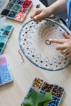Closeup woman artist creating handmade accessory dreamcatcher use colorful beads amulet for luckの写真素材