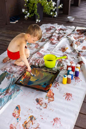 Little boy draws with hands and feet with finger paints on a large sheet at homeの写真素材