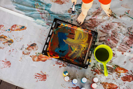 Little boy draws with hands and feet with finger paints on a large sheet at homeの写真素材