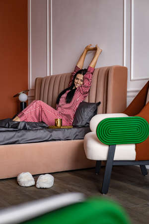 Adorable female stretching body with raised hands lying on bed lazy morning with positive emotion