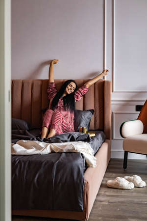 Adorable female stretching body with raised hands lying on bed lazy morning with positive emotionの写真素材