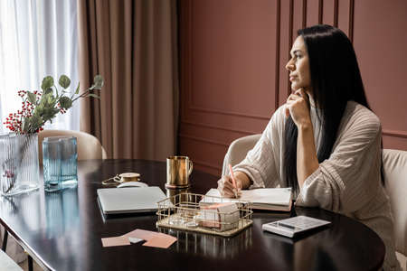 Smiling beauty woman writing diary paper notes planning job business sitting at comfy home office