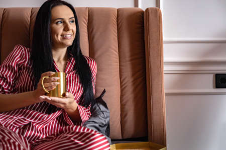 Closeup beauty female hands in pajamas holding golden metallic mug with hot beverage relaxing on bedの写真素材