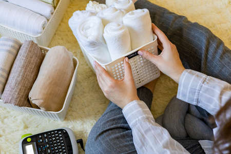 Woman hands neatly folded linens and towels use Marie Kondo method with sticky label tagsの写真素材