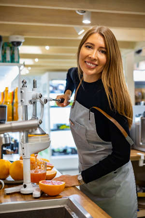 Portrait smiling woman bartender in apron cooking healthy detox refreshing juice orange grapefruitsの写真素材
