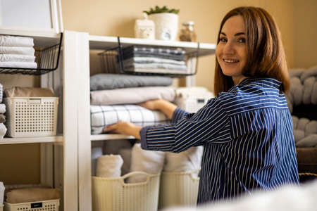 Domestic woman in pajamas neatly putting folded linens into cupboard vertical storage Marie Kondoの写真素材