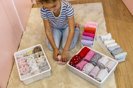 Happy girl neatly roll folded underwear and socks in plastic container box
