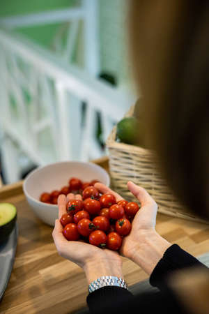 Top view farmer female hands holding bowl with small ripe cherry tomatoes and fresh green avocado
