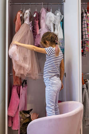 Cute little girl choosing festive dress hanged in pink cupboard comfortable clothes vertical storageの写真素材
