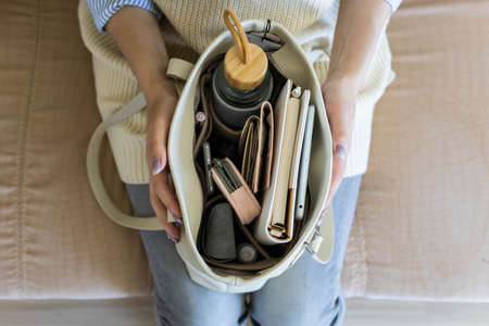 Top view closeup female hands holding modern handbag full of personal accessories in felt storage