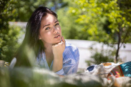 Portrait of beautiful Japanese woman posing with notepad lying on plaid at summer garden park
