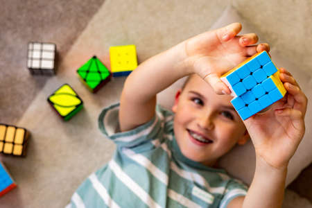 Top view happy male kid assembling multicolored mind logical toy Rubiks cube with positive emotionのeditorial素材