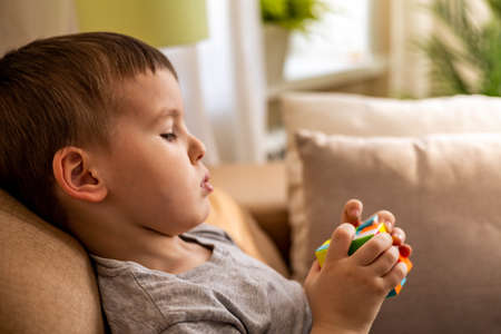 Cute baby boy assembling multicolored Rubiks cube solving logical game lying on couch at homeのeditorial素材
